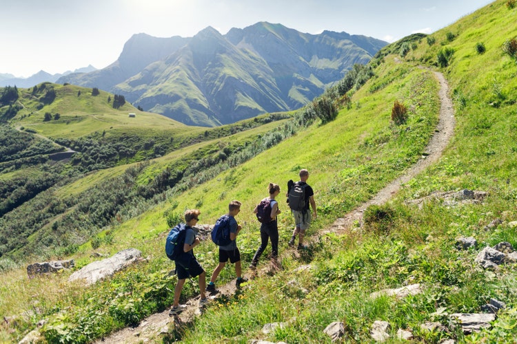 Four people hike up on a green hillside with mountains