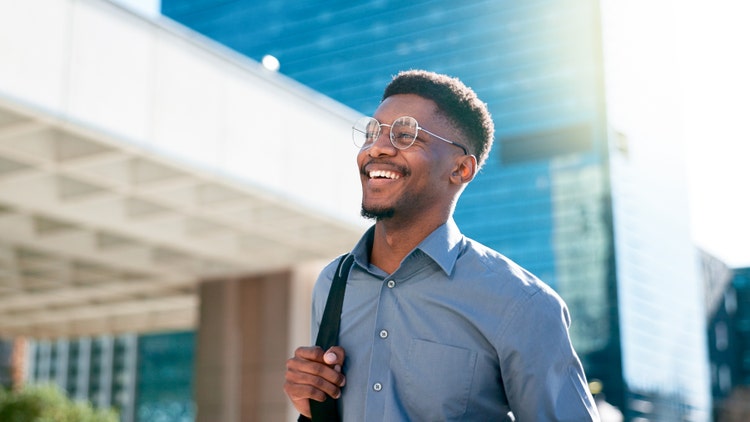 A young man smiles while walking outdoors with a backpack